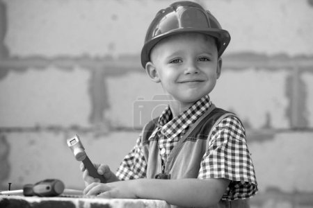 Photo for Cute little kid in builder helmet with repair tools on construction site. Child boy in a construction helmet working hard. Happy smiling kids education and career. Kids builder and repair - Royalty Free Image