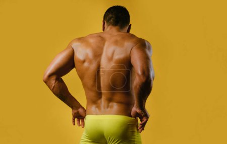 Photo for Sexy male back. The back view of torso of attractive male body builder on yellow background. Rear view of a bare-chested muscular young man in sexy panties underwear - Royalty Free Image