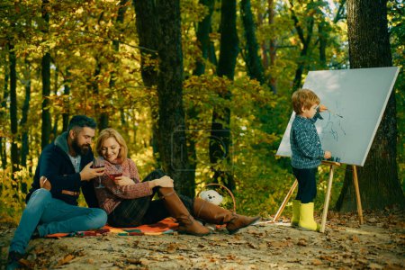 Photo for Painting skills. Mom and dad relax park picnic while kid painting. Rest and hobby concept. Parents watching their little son painting picture in nature. Art and self expression. Talent development. - Royalty Free Image