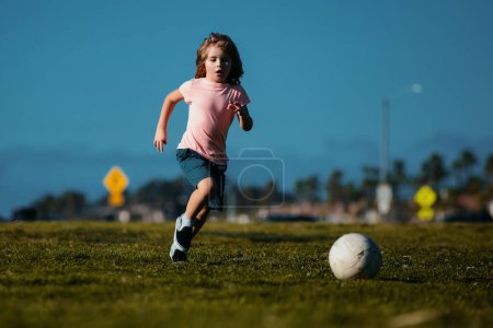 Téléchargez les photos : Excited child boy kicking ball in the grass outdoors. Soccer kids, children play football - en image libre de droit