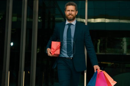 Téléchargez les photos : Homme d'affaires faisant du shopping en ville. Portrait d'homme d'affaires en costume avec sacs à provisions - en image libre de droit