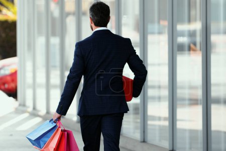 Téléchargez les photos : Vue arrière de l'homme d'affaires posant avec des sacs à provisions en plein air - en image libre de droit