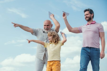 Photo for Active family leisure with kids. Boy son with father and grandfather with a toy airplane plays on summer sky background - Royalty Free Image