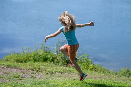 Téléchargez les photos : Petit garçon courant sur l'herbe verte près du lac dans le parc d'été. Enfant garçon jouer et courir dans le parc d'été - en image libre de droit