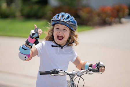 Téléchargez les photos : Petit garçon en vélo dans un parc d'été. Les enfants apprennent à conduire un vélo sur une allée à l'extérieur. Enfant à vélo dans la ville portant des casques comme équipement de protection. Enfant à vélo extérieur - en image libre de droit