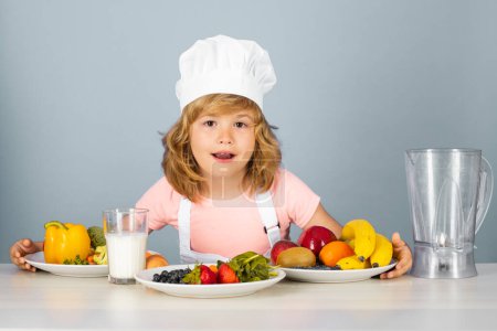 Photo for Child wearing cooker uniform and chef hat preparing vegetables on kitchen, studio portrait. Cooking, culinary and kids food concept - Royalty Free Image