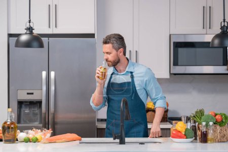 Téléchargez les photos : Homme en tablier de cuisine cuisine alimentaire avec bouteille d'huile d'olive dans la cuisine. Cuisiner dans tablier de chef sur cuisine avec bouteille d'huile d'olive - en image libre de droit