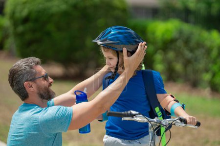 Photo for Father teaching son riding bike. Dad helping child son to ride a bicycle in american neighborhood. Father helping his son to wear a cycling helmet. Happy fathers day. Summer sport with child - Royalty Free Image