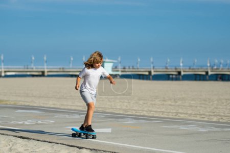 Foto de Kid boy riding skateboard in the road. Kid practicing skateboard. Children learn to ride skateboard in a park on sunny summer day. Active leisure and outdoor sport for child - Imagen libre de derechos