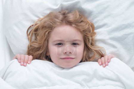 Photo for Kid under covers, face cover with blanket. Child wakes up from sleep in bed. Kid wakes up in the morning in the bedroom. Healthy sleeping, zzz concept - Royalty Free Image