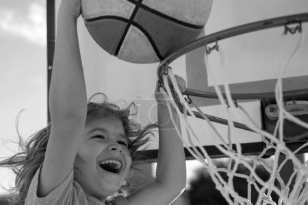 Téléchargez les photos : Petit sportif caucasien jouant au basket en tenant le ballon avec un visage heureux. drôle excité visage d'enfant - en image libre de droit