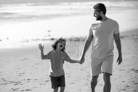 Téléchargez les photos : Joyeux concept de famille. Père et fils marchant sur la plage d'été. Papa et enfant garçon tenant la main et marcher ensemble - en image libre de droit