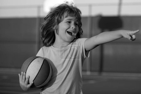 Foto de Feliz niño sonriente jugando baloncesto, apuntando mostrando gesto. Actividad y deporte para niños - Imagen libre de derechos