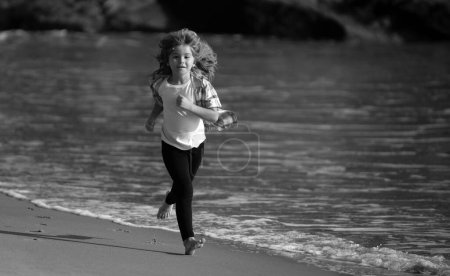 Téléchargez les photos : Le gamin court sur la plage. Joyeux enfant courir en mer pendant les vacances d'été. Petit athlète en entraînement. Exercice du coureur, jogging pour les enfants - en image libre de droit