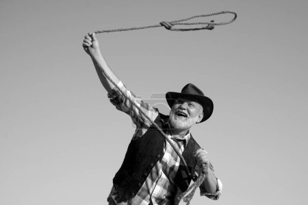 Téléchargez les photos : Vieux cow-boy sauvage de l'ouest au rodéo. Pensionné occidental avec corde à lasso. Homme barbu avec veste brune et chapeau attrapant cheval ou vache - en image libre de droit