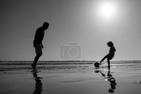 Photo for Father and son play soccer or football on the beach on summer family holidays - Royalty Free Image