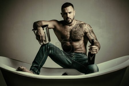single man drink champagne from bottle. cold alcohol with ice bucket. brutal sportsman torso. sport and fitness, health. sexy abs of tattoo man. male loneliness. muscular macho man with athletic body.