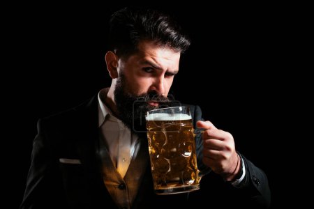 Foto de Hipster con barba y bigote en traje bebe cerveza después de la jornada laboral. Alemania Baviera. Hora de la cerveza. Barman guapo sosteniendo una pinta de cerveza - Imagen libre de derechos