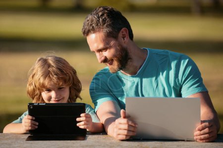 Photo for Online learning. Happy father using laptop relax with schooler son holding laptop have fun together, smiling dad and little boy child enjoy weekend with gadgets outside on nature - Royalty Free Image