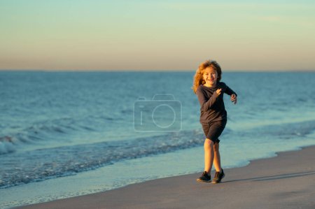 Foto de Niño feliz corriendo en la playa del mar. Chico gracioso corre a lo largo del borde del surf. Estilo de vida infantil activo - Imagen libre de derechos