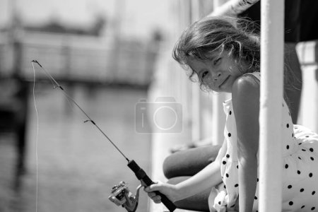 Foto de Graciosa niña pequeña coger un pez por una caña de pescar - Imagen libre de derechos
