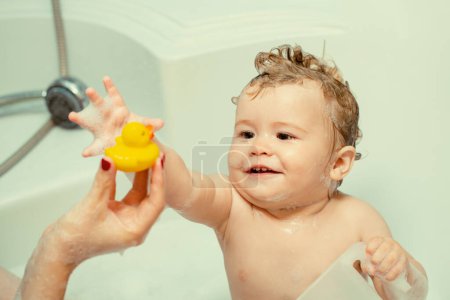 Photo for Kid bathing in bathtub. Funny happy baby bathes in bathtub with water and foam. Kids hygiene. Smiling kid in bathroom with toy duck - Royalty Free Image