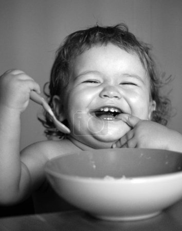 Téléchargez les photos : Joyeux lancement bébé se manger avec une cuillère. Lécher les doigts savoureux - en image libre de droit