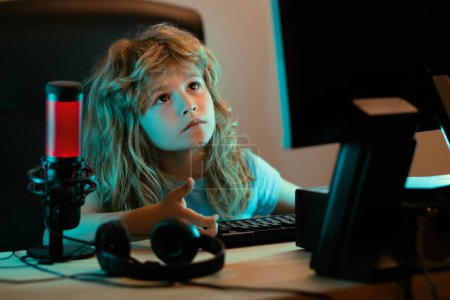 Téléchargez les photos : Enfant avec ordinateur PC la nuit. Un joli enfant apprend une leçon à l'aide d'un ordinateur de bureau à la maison. Enseignement à domicile - en image libre de droit