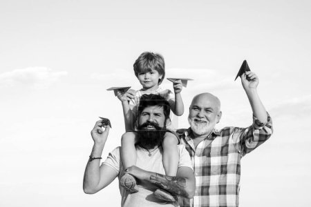 Téléchargez les photos : Joyeuse fête des pères. Heureux trois générations d'hommes s'amusent et sourient sur fond de ciel bleu. Grand-père jouant. Avion prêt à voler - en image libre de droit