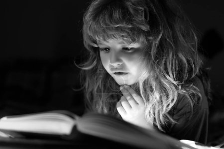 Téléchargez les photos : Enfant lisant un livre au lit avant d'aller dormir. Petit garçon allongé sur le lit lisant le livre à la maison. Concept d'éducation et de lecture - en image libre de droit