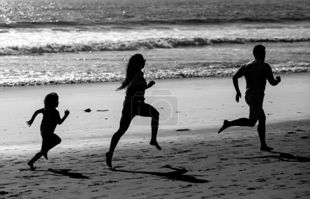 Foto de Familia de fitness corriendo en una playa de arena. Deportivo padre de familia, madre e hijo bebé corriendo juntos. Niño con padres regados por el agua a lo largo del mar. Deporte, salud en verano. Estilo de vida saludable - Imagen libre de derechos