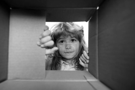 Photo for Surprised child boy unpacking, opening carton box and looking inside. The package, delivery, surprise, gift for kid. Children emotions and kids facial expressions concepts - Royalty Free Image
