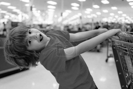 Téléchargez les photos : Un garçon fait du shopping dans un supermarché. Enfant drôle avec chariot avec dans l'épicerie - en image libre de droit