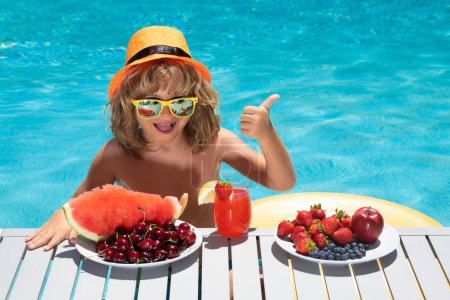 Téléchargez les photos : Portrait d'enfants d'été. Enfant avec des fruits et jus smoothie cocktail dans la piscine d'été. Enfant en vacances d'été. Fruits d'été pour enfants - en image libre de droit