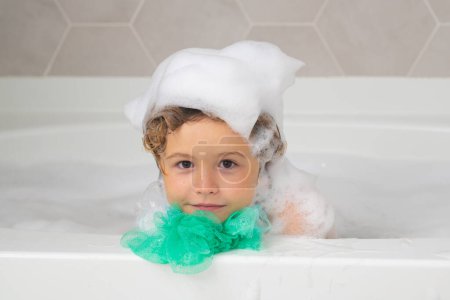 Photo for Foam on kids head. Soap on child head. Child boy washing with a bubbles in bath. Cute child bathes, lying in a white bath with foam from soap and shampoo - Royalty Free Image
