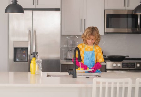 Téléchargez les photos : Une femme de ménage. Lavage et essuyage des enfants dans la cuisine. Un gamin américain qui apprend les tâches domestiques à la maison. Nettoyage des enfants pour aider les parents avec la routine de ménage. Concept d'enfants de ménage - en image libre de droit