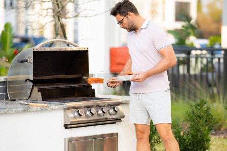 Photo for Man cooking meat on barbecue in the backyard of the house. Handsome man preparing barbecue. Barbecue chef master. Cook preparing delicious grilled barbecue salmon fillet, bbq meat. Grill and barbeque - Royalty Free Image