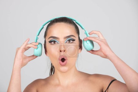 Foto de Mujer joven emocionada escuchar música con auriculares, bailando. Chica escuchando música usando auriculares inalámbricos aislados sobre fondo de estudio - Imagen libre de derechos