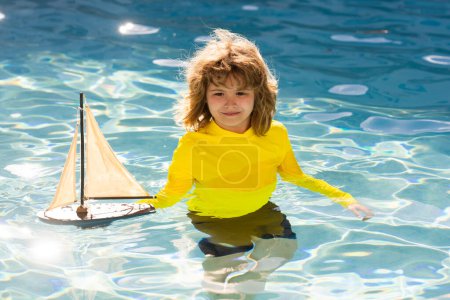 Téléchargez les photos : Enfant jouant avec le voilier jouet sur la plage de la mer à l'heure du coucher du soleil d'été. Silhouette coucher de soleil d'un enfant garçon rêvant en croisière. Rêver de voyager. gamin jouant avec un voilier jouet. Journée des enfants - en image libre de droit