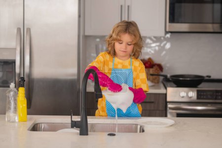 Téléchargez les photos : Concept de lavage de vaisselle. Mignon enfant aide à laver la vaisselle à la cuisine. Nettoyage des enfants de kithen aider avec les travaux ménagers. Mignon enfant garçon ménage, maison propre enfant - en image libre de droit