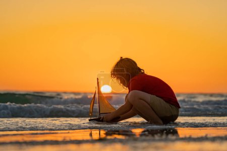 Photo for Child playing with a toy boat. Little kid boy sailing toy ship on sea water. Summer vacation with kids. Kid dreaming about sailing. Concept of childhood and family vacation. Travel with children - Royalty Free Image