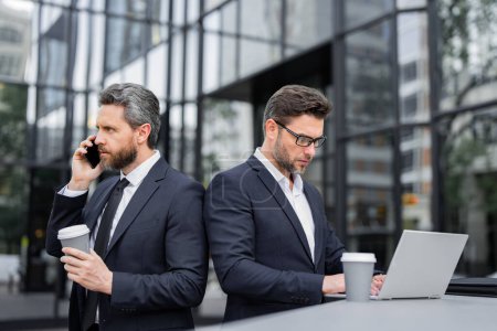 Photo for Business teams with takeaway coffee, mobile phone and laptop outdoor. Business men team using laptop and phone outdoor. Businessmen looking laptop with their business success in city background - Royalty Free Image