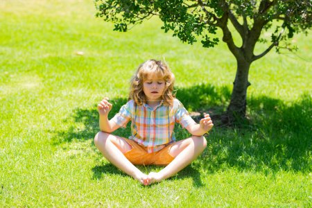 Téléchargez les photos : Enfant faisant du yoga pose dans le parc en plein air. Calme et détente. Enfant médite tout en pratiquant le yoga. Méditation de pleine conscience. Garçon détendu avec les yeux fermés respirer l'air frais à l'extérieur, profiter de la nature - en image libre de droit