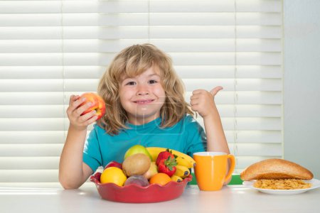 Photo for Kid eating apple. Schoolchild eating breakfast before school. Portrait of little teen child sit at desk at home kitchen have delicious tasty nutritious breakfast - Royalty Free Image