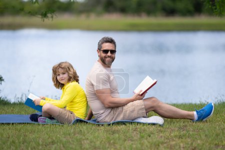 Photo for Father reading book with son in park, preparing school homework together, parenting. Summer lifestyle. Parenting and childhood concept. Little boy learning with father in outdoors garden - Royalty Free Image