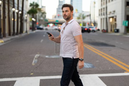 Photo for Portrait of handsome man chatting on phone outdoor. Stylish man talking on phone dressed in polo. Fashion male posing on the city street. Urban style. Business phone conversation - Royalty Free Image