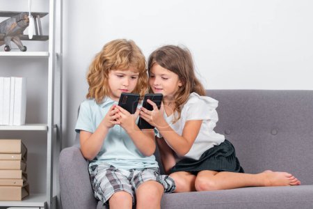 Téléchargez les photos : Les enfants jouent au smartphone. Frère et sœur à la maison jouant à des jeux vidéo. Deux frères et sœurs frère soeur à la maison seul en utilisant le téléphone mobile. Enfants jouant à des jeux vidéo sur gadget. Dépendance aux médias sociaux - en image libre de droit