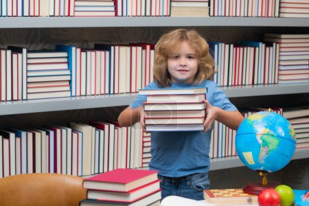 Téléchargez les photos : Un écolier avec une pile de livres à la bibliothèque. Concept scolaire et éducatif. Portrait de mignon enfant écolier. Retour à l'école - en image libre de droit