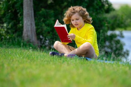 Photo for Cute little boy reading book in park. Kid sit on grass and reading book. Kid boy reading interest book in the garden. Summertime fun. Cute boy reading a kids book - Royalty Free Image