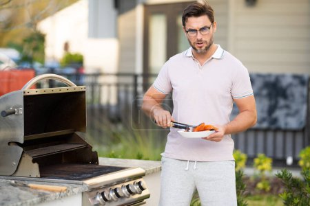 Photo for Man at a barbecue grill. Male cook preparing barbecue outdoors. Bbq salmon fillet, grill for picnic. Roasted beef. Cook preparing barbeque in the house yard. Barbecue and grill - Royalty Free Image